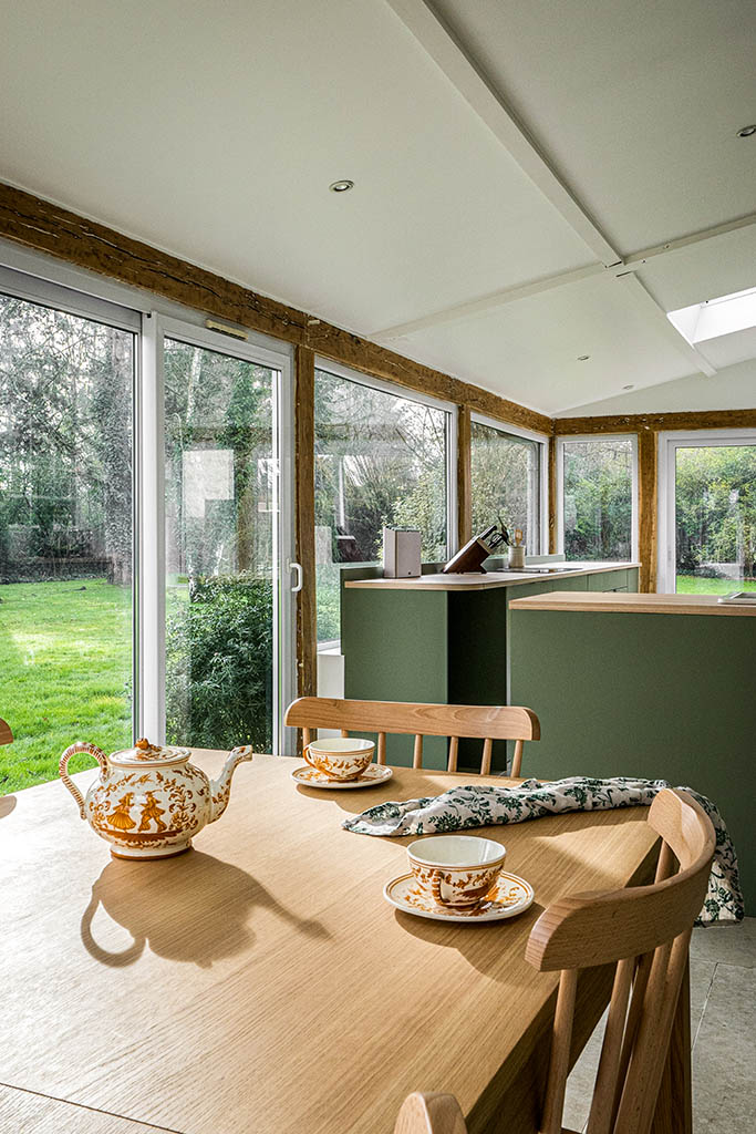 Linéaire cuisine verte avec plan de travail bois, sol pierre ancienne, carrelage mural zellige blanc, poutres poncées bois apparent