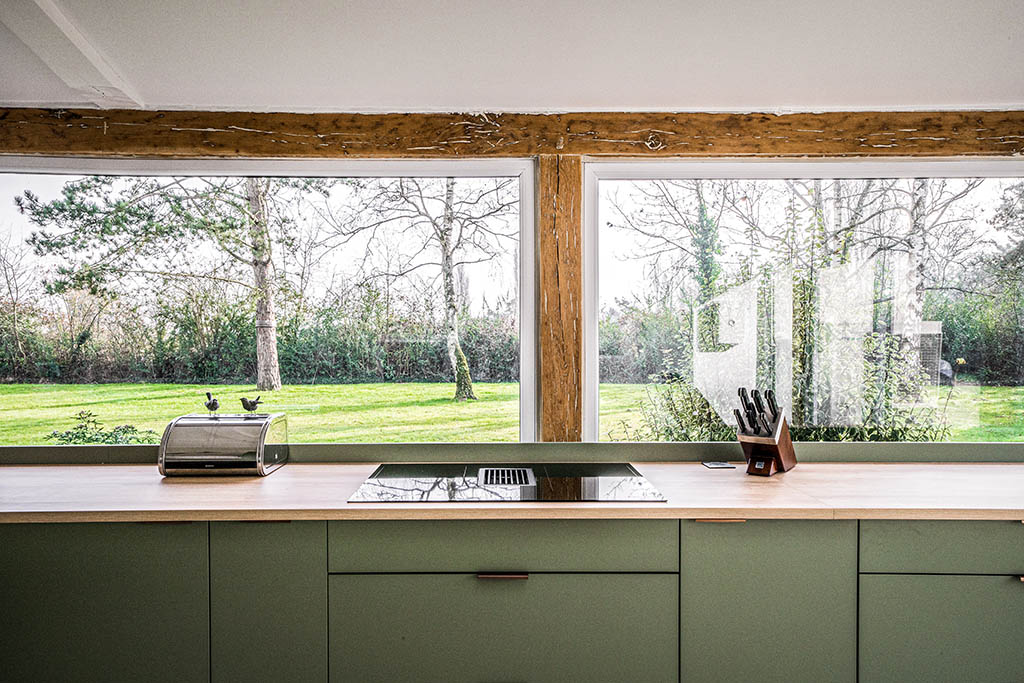 Linéaire cuisine verte avec plan de travail bois, sol pierre ancienne, carrelage mural zellige blanc, poutres poncées bois apparent