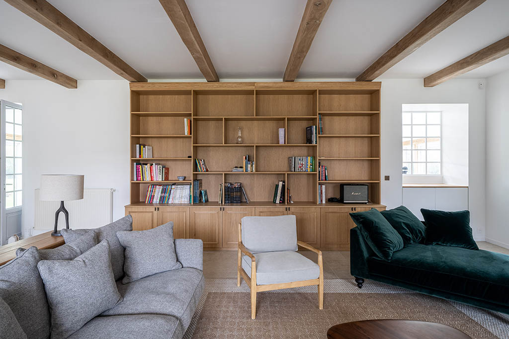 Meuble bibliothèque en bois sur mesure avec rangements bas fermés et partie haute ouverte avec LEDS dans séjour esprit campagne moderne avec poutres en bois