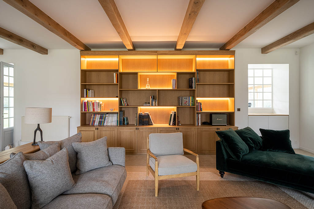 Meuble bibliothèque en bois sur mesure avec rangements bas fermés et partie haute ouverte avec LEDS dans séjour esprit campagne moderne avec poutres en bois