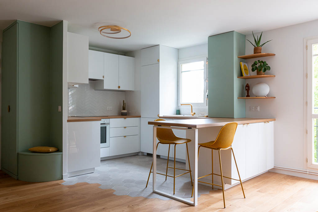 Linéaire cuisine esprit scandinave épuré blanche et verte avec plan de travail bois avec bar déporté, coffrage et étagères bois sur mesure, robinetterie et poignées laiton, crédence blanche chevron et carrelage sol tomettes